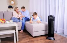 Oczyszczacz powietrza Ionic-CARE v obývacím pokoji, v pozadí rodina relaxující na světlé pohovce u okna, barva černá